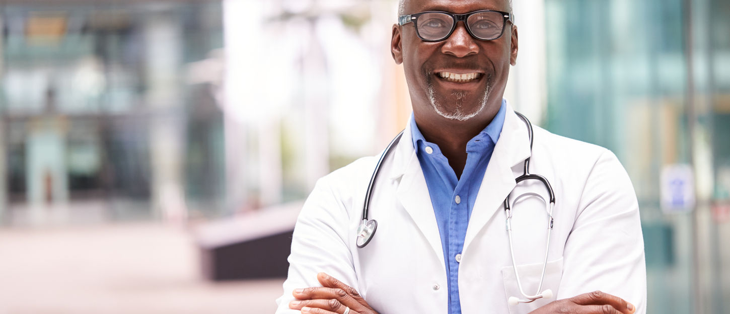 Portrait Of Male Doctor With Stethoscope Wearing White Coat Standing In Modern Hospital Bu