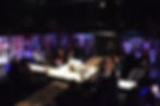 A theatre with a platform running through it vertically and horizontally. On the walls are various bits of paper, getting darker the further into the theatre they get.