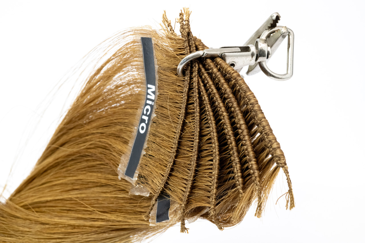 A close up of Gold Class hand-tied weft samples attached to a metal clip, showing a range of weft densities from Micro upward, with visible stitching and track thickness differences.
