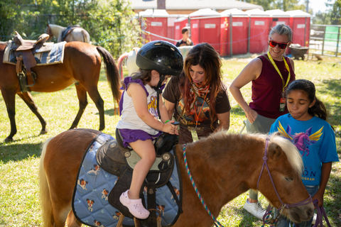 Young child in helmet on a pony, supervised by adults