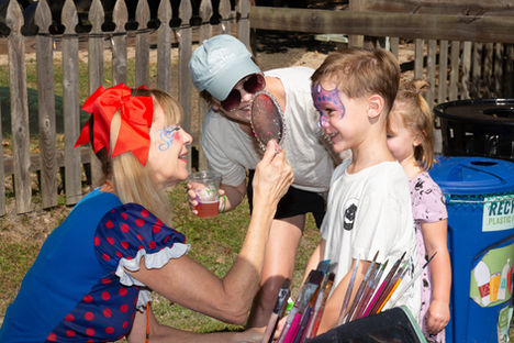Face painter applies design to boy's face, woman holds mirror