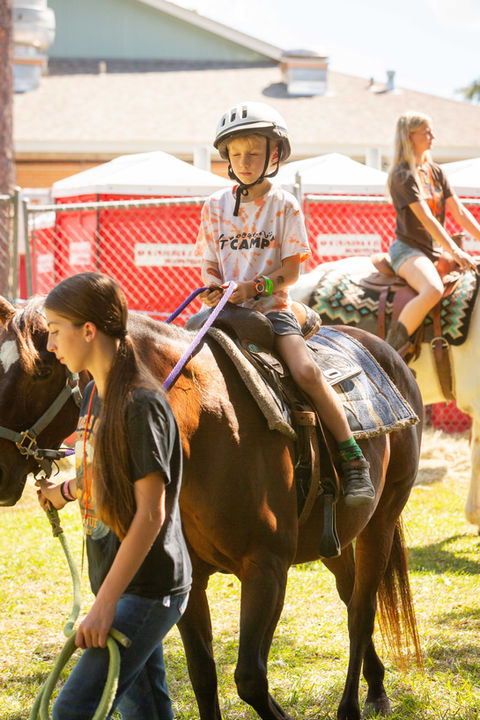 Boy in helmet riding a horse, led by a girl