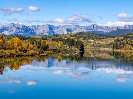 Calm mountain lake reflecting autumn trees and the Canadian Rockies under a blue sky – nature photography by Moments by Giselle.