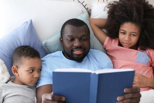 african-american-man-reading-bedtime-story-to-his-children-in-bed-photo.jpg