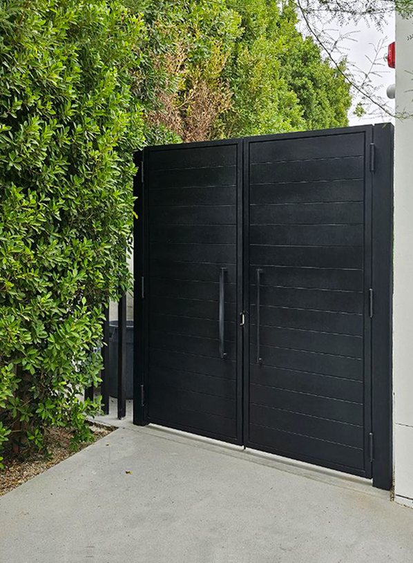 Black metal gate entrance leading to a residential property with lush trees.