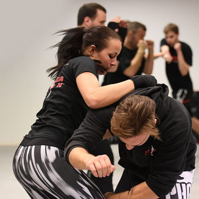 Frau führt Knie Stoß im Krav Maga Training aus und trägt schwarzes Defcon T-Shirt in der Kampfsportschule Filderstadt