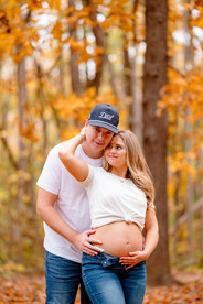 Couple embracing by a lake in autumn, surrounded by colorful leaves. The woman wears a brown dress; the man wears a plaid shirt and jeans. Romantic mood. Jetton Park on Lake Norman.