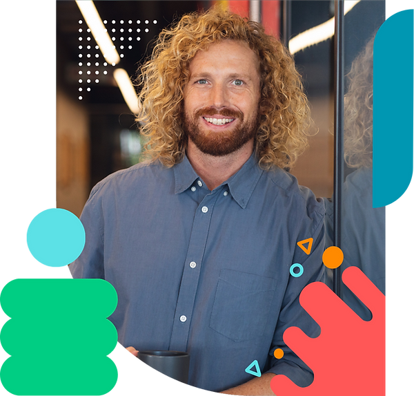 A man with long, curly blond hair smiles in an office, surrounded by abstract, colorful shapes.
