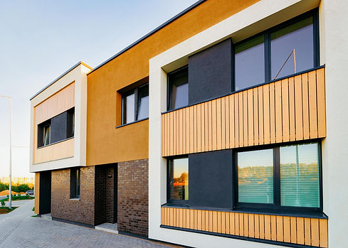 A low-angle exterior view of a modern multi-family residential building featuring a contemporary facade with orange stucco, dark brick, wood paneling accents, and large windows.