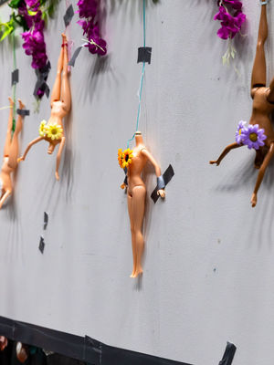 Headless play dolls hang on a wall, covered in flowers.