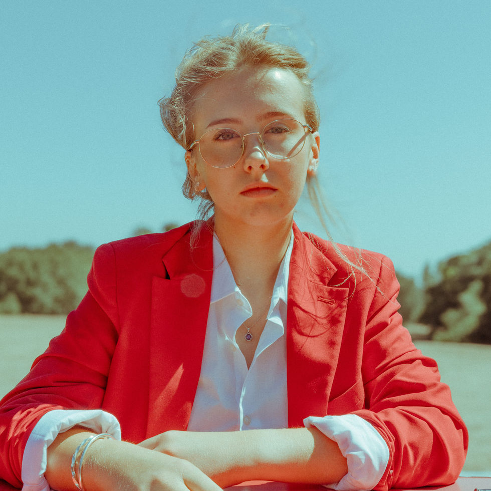 A young woman dressed in red, stares straight down a camera.