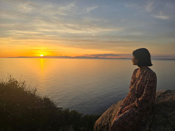 Una ragazza che guarda il tramonto sul mare seduta su una roccia