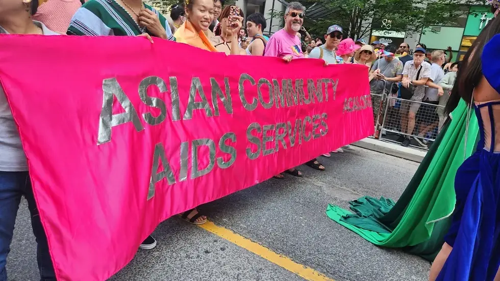 People holding an Asian Community AIDS Services banner at a parade.