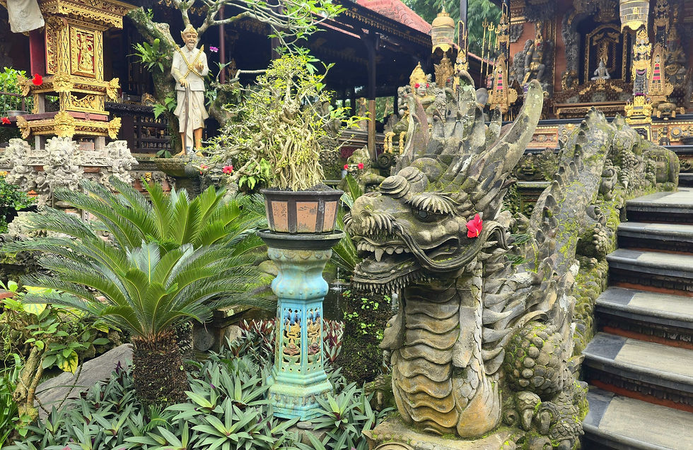 Ornate stone dragon statue with red flowers, lush greenery, and a traditional statue in an elaborate temple setting.