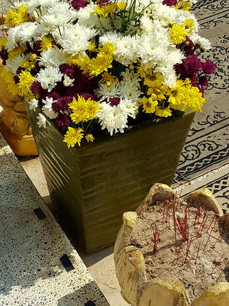 A brown bucket full of colourful flowers and a bowl of incense sticks