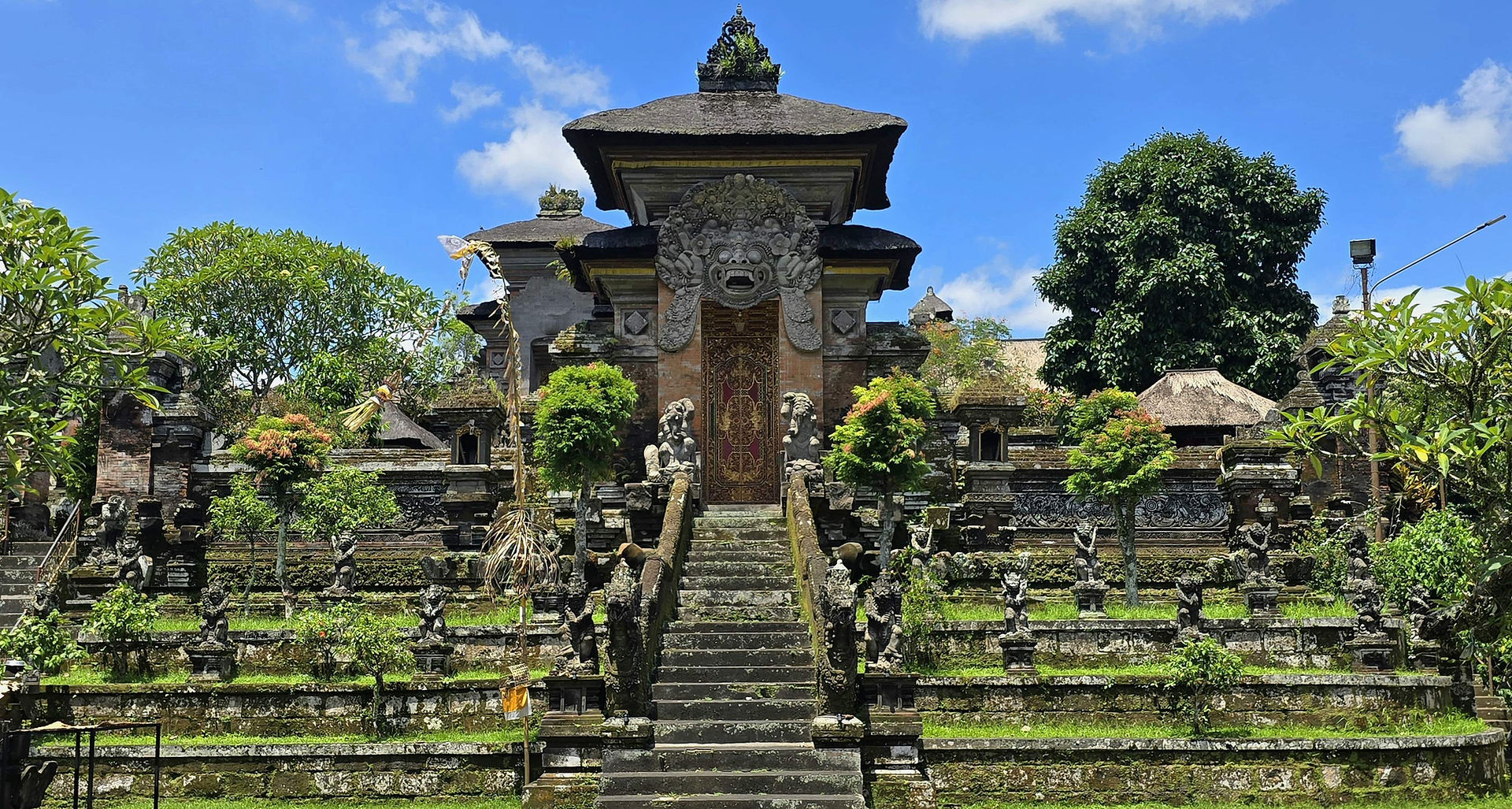 Traditional temple surrounded by mossy green statues and a large steep staircase leading to the main gate