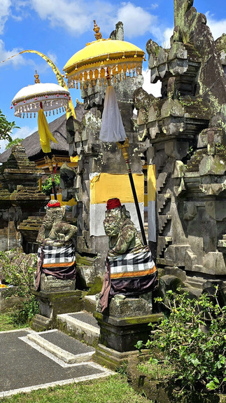 Balinese temple stone guardians with yellow and white ceremonial umbrellas under a bright blue sky.