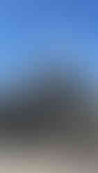 Ancient stone temple with intricate carvings stands against a bright blue sky. Scattered stone blocks in the foreground add texture.