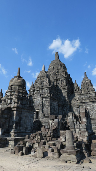 Ancient stone temple with intricate carvings stands against a bright blue sky. Scattered stone blocks in the foreground add texture.