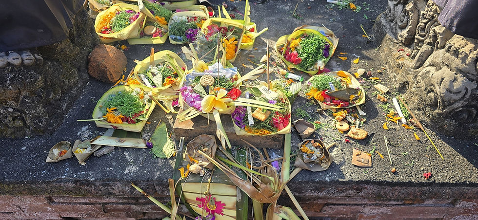 Colourful flower-and-rice offerings in woven palm-leaf baskets on a stone altar, with incense and scattered petals.