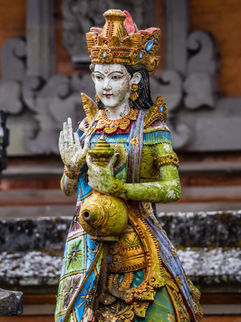 Colourful statue of Dewi Danu with orange and grey stone temple in the background