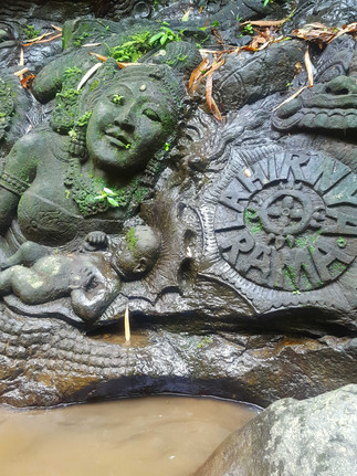 Stone relief of a mother and child with moss accents. Intricate carvings and visible text "AHIRMA RAMA". Set against a wet rock background.