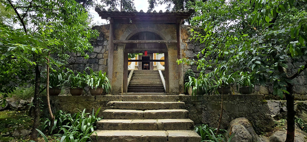 Stone steps lead to an ancient archway framed by lush greenery. Potted plants line the path, with a serene, historical ambiance.