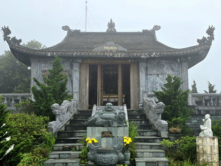 Misty temple facade with intricate dragon designs, stone statues, and yellow flowers. Lush greenery surrounds the stairs. Tranquil atmosphere.