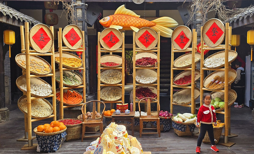 Child in red sweater stands by bamboo shelves with assorted dried goods and vegetables in a marketplace, featuring a large fish decoration.