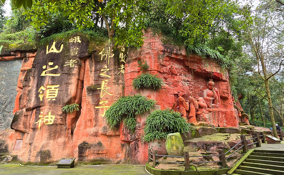 Red rock carving of figures with green foliage; yellow Chinese characters on the rock surface; serene forest setting.