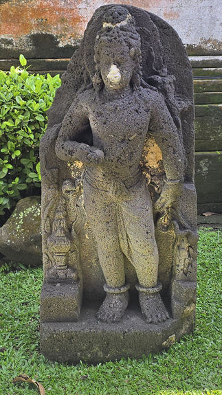 Stone statues of figures pouring water into a pond, ornate carvings, lush greenery. Red-tiled roof and clear blue sky in the background.