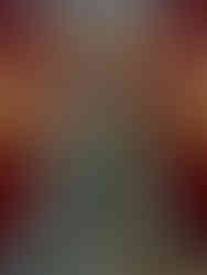 Intricately carved green statue of a seated figure in a serene pose inside a glass case, against a warm-toned, ornate background.