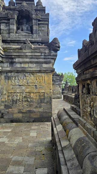 Ancient stone temple with intricate carvings and statues, under a cloudy blue sky. Moss-covered bricks line the pathway, evoking historical serenity.