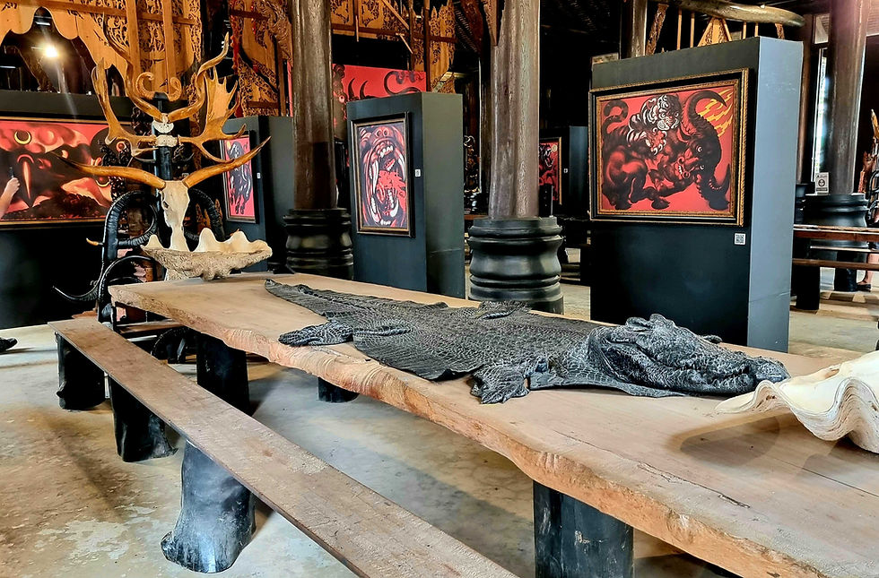 Dark art gallery with wooden benches, crocodile sculpture, antlers, and red-black paintings in an ornate hall.