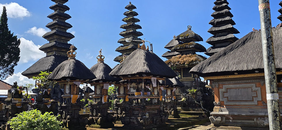 Balinese temple courtyard with thatched shrines and tall tiered meru towers under a bright blue sky