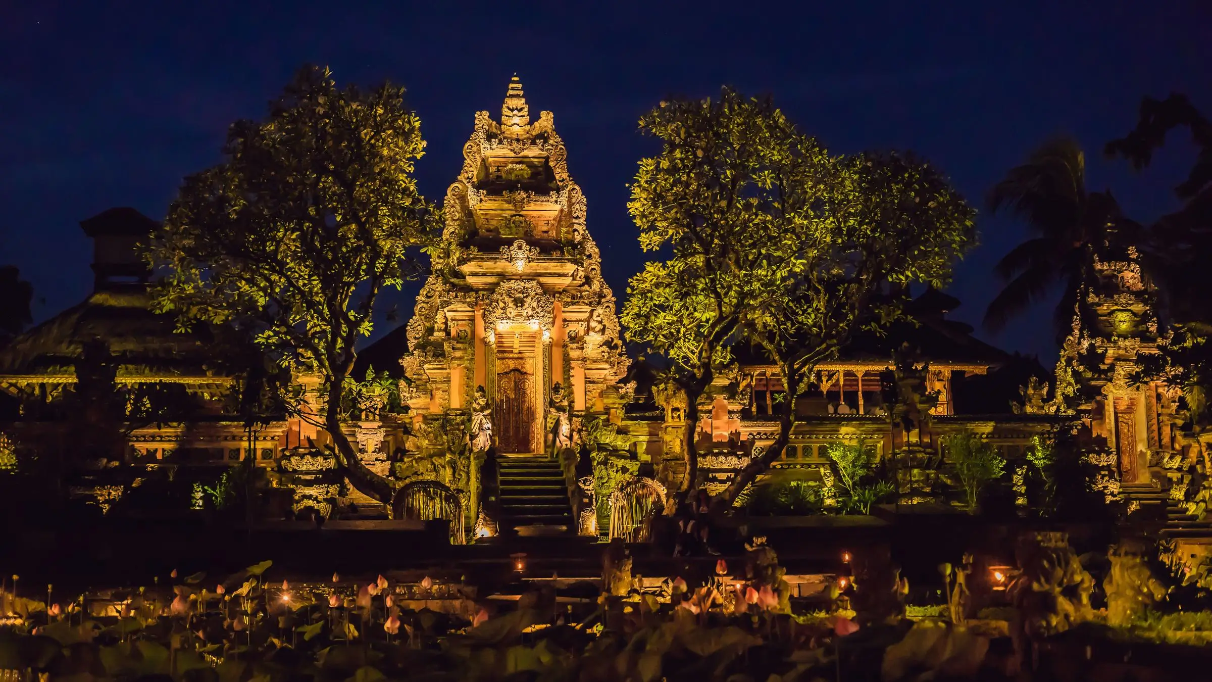 Illuminated temple at night, surrounded by trees and lit by soft yellow lights. Dark sky creates a serene, mystical atmosphere.