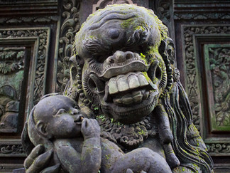 Mossy stone statue of Rangda, bearing teeth and holding a baby