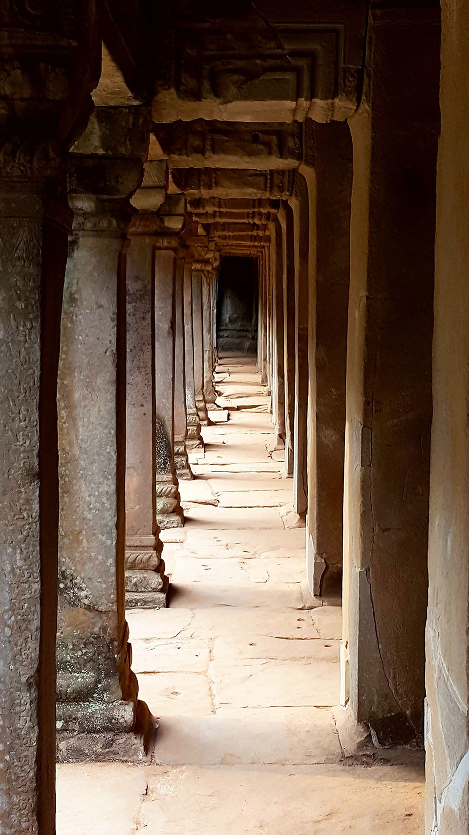 Narrow rectangular stone corridor inside Ta Prohm Temple, with worn sandstone walls and a dim, atmospheric glow