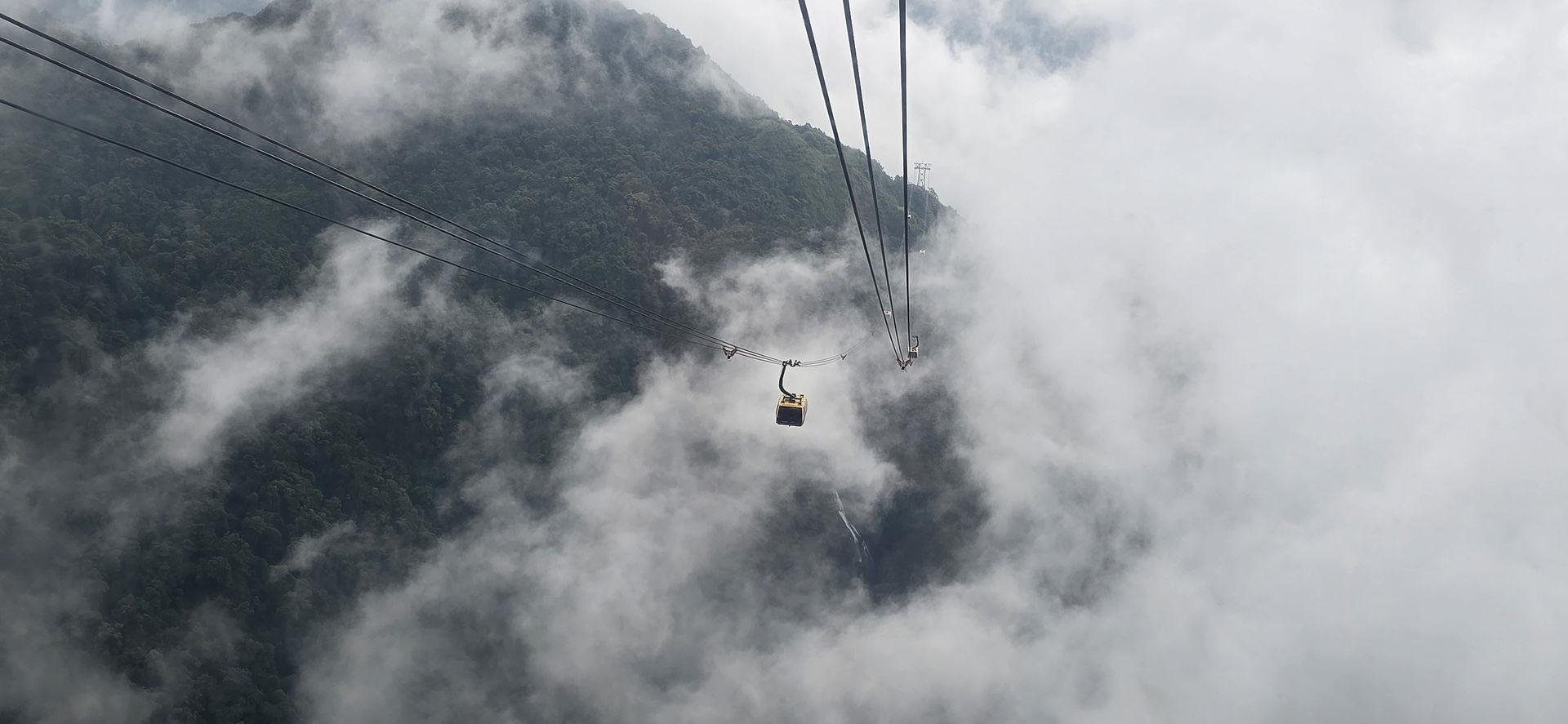 A yellow cable car travels through misty clouds over a lush green mountain landscape, evoking an adventurous and serene mood.