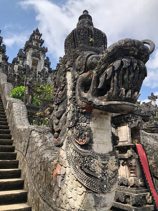 Ornate stone dragon sculpture on temple stairs with intricate carvings and details. Cloudy sky background, lush greenery around.