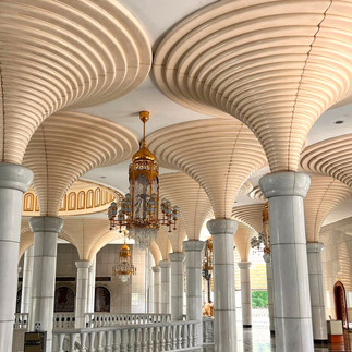 Ornate interior with spiral white columns, gold chandeliers, and arched windows. Bright, elegant ambiance with intricate designs.