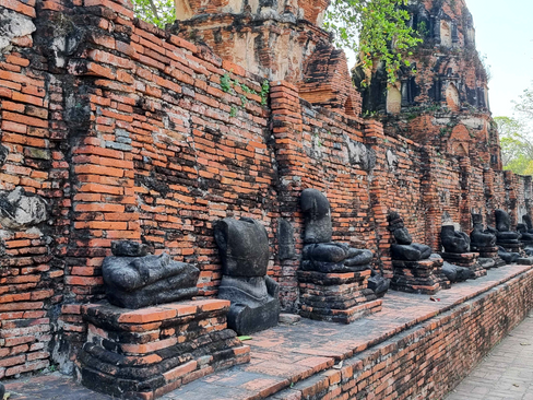A row of headless black statues along an ancient orange stone fence