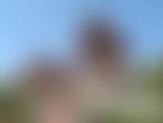 Ornate Thai temple with red roofs and intricate carvings under a clear blue sky. Sculpted steps lead up, surrounded by lush greenery.