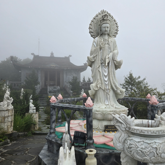 A large stone statue stands in a misty temple garden, surrounded by smaller statues and trees. A foggy atmosphere enhances the serene mood.