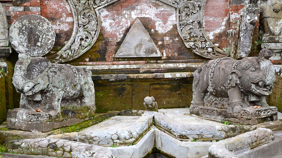Stone elephant statues on a mossy, ornate temple wall. Brick and intricate carvings adorn the background, creating an ancient ambiance.