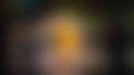 A curved white moon-gate bridge, glowing with warm light, casting a glow on the water, green trees in the background