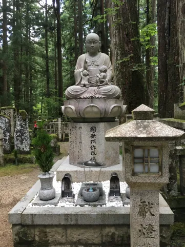 Stone statue of a buddha on a lotus flower, stone lantern with Japanese calligraphy, several small stone jars with offerings and incense 