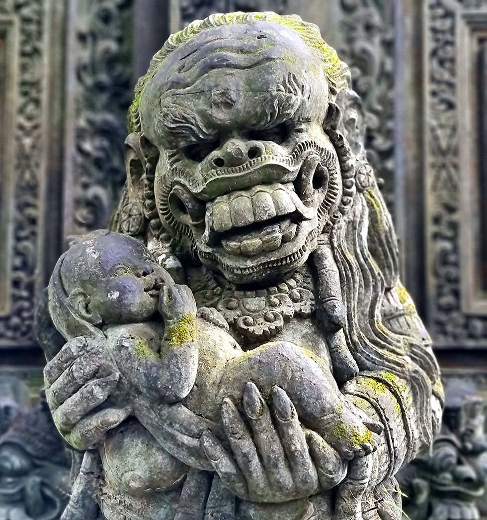 Stone statue of a fierce figure cradling a baby, featuring intricate carvings and moss. Background shows detailed ornate patterns.