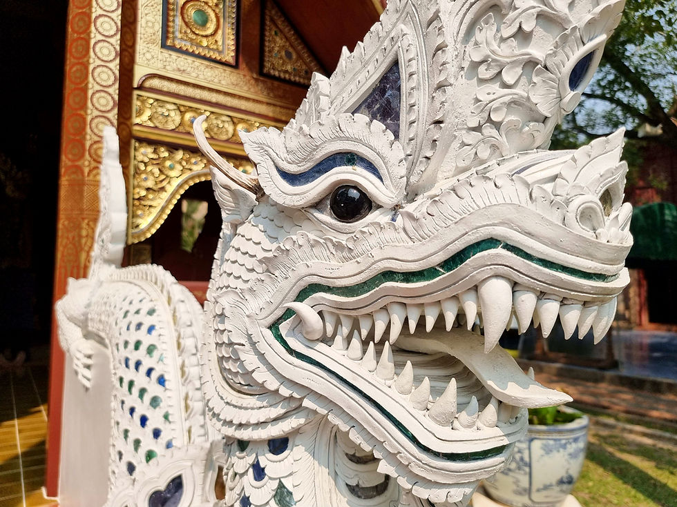 White ornate dragon statue with intricate scales and blue-green details at a temple entrance, set against a richly decorated golden background.