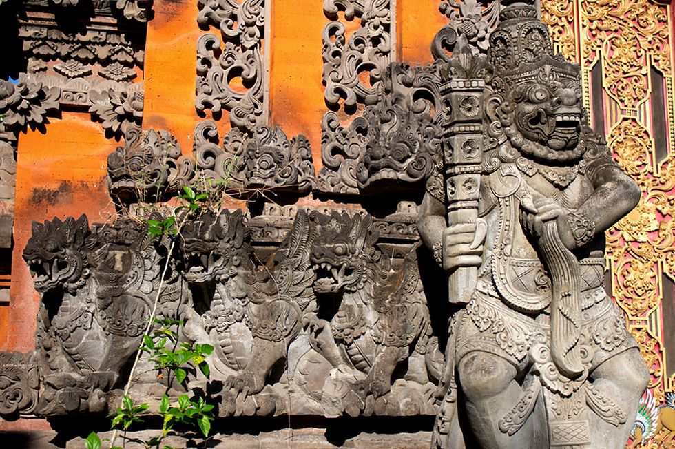 Ornate stone carvings of mythical creatures and a fierce guardian statue on an orange and gold temple wall with intricate patterns.